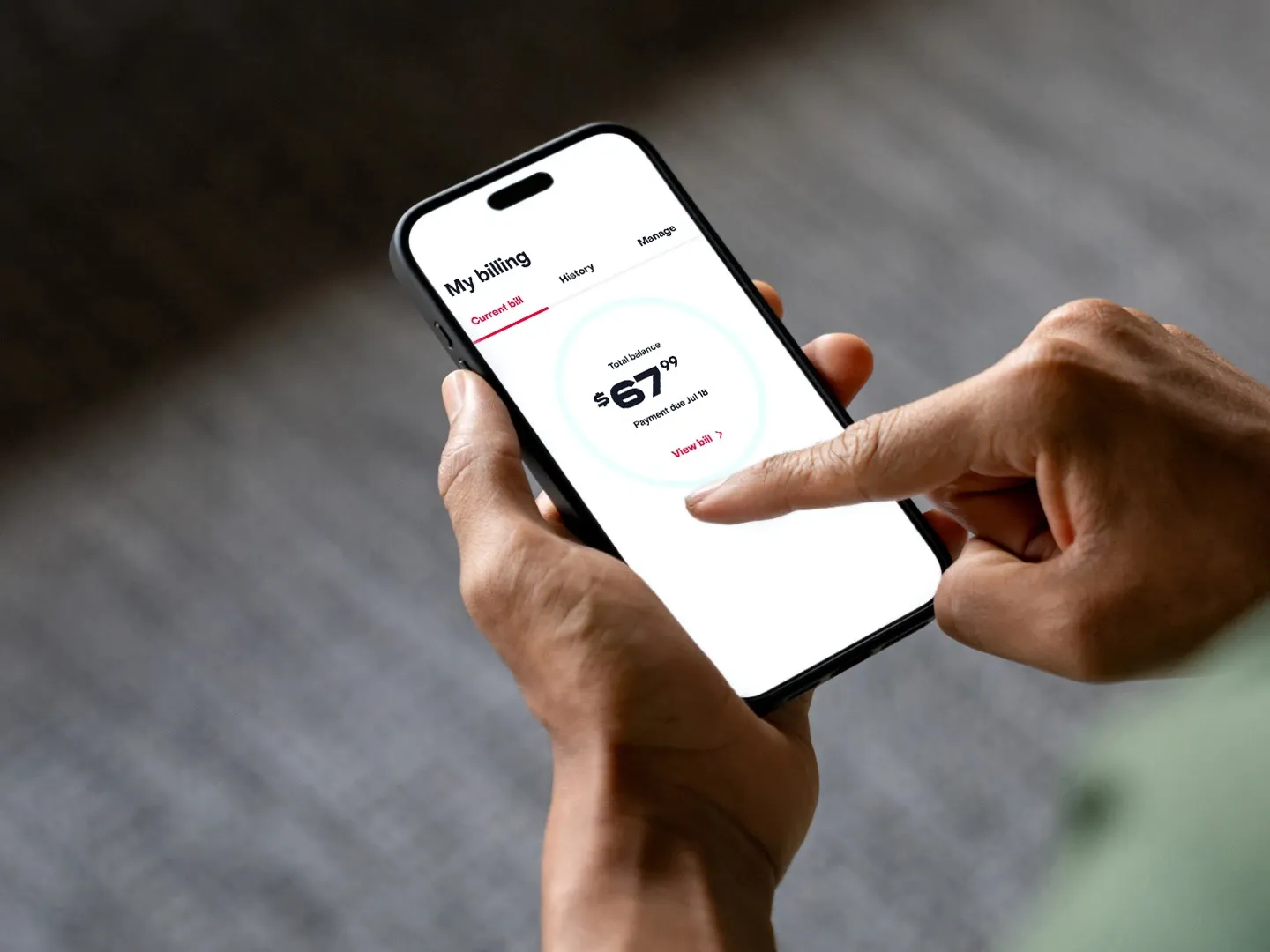 A person holding a smartphone displaying a billing interface with a total balance of sixty-seven dollars and ninety-nine cents.
